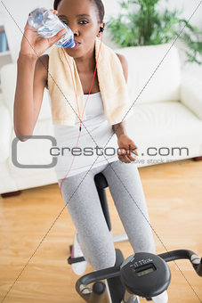 Black woman sitting on an exercise bike while drinking