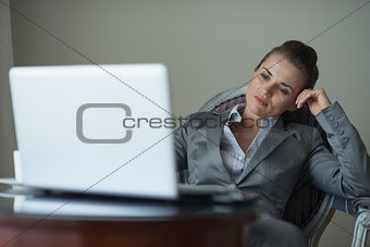 Tired business woman sitting in hotel room and looking on laptop