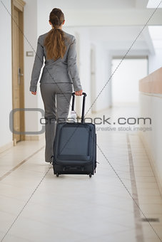 Business woman walking with bag on wheels. rear view