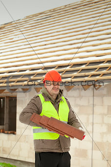 Builder with roof tiles near new building
