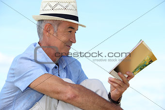 A mature man reading a book outside.