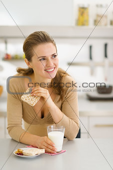 Young woman eating snacks in modern kitchen and looking on copy 