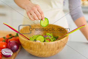 Closeup on housewife adding cucumber into vegetable salad