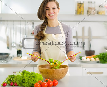Happy young housewife mixing vegetable salad