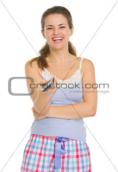 Smiling Young woman in pajamas holding TV remote control