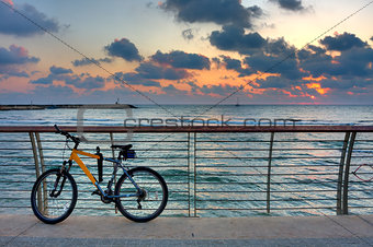 Bike on promenade against background of sunset sky and sea.