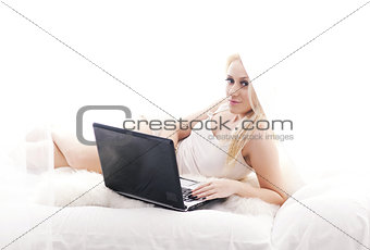 Blonde girl with laptop lying in bed