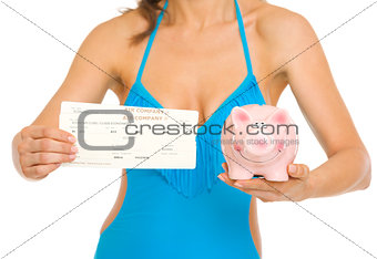 Closeup on young woman in swimsuit showing air tickets and piggy