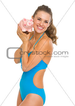 Happy young woman in swimsuit showing piggy bank