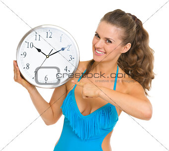 Smiling young woman in swimsuit pointing on clock
