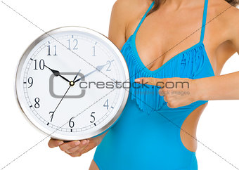 Closeup on young woman in swimsuit pointing on clock