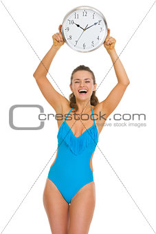 Smiling young woman in swimsuit showing clock