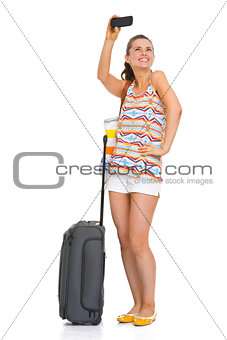 Happy young tourist woman with wheel bag taking self photo