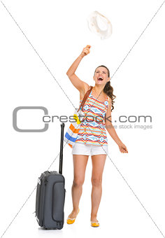 Happy young tourist woman with wheel bag throws up hat