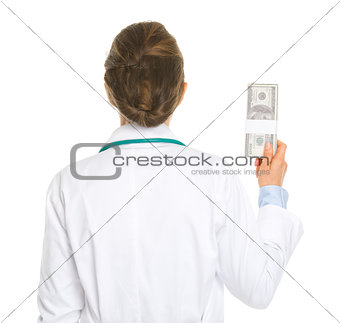 Medical doctor woman holding pack of dollars . rear view
