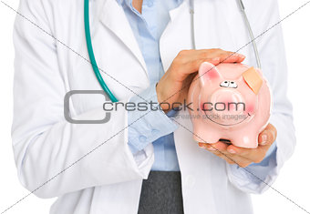 Closeup on medical doctor woman holding piggy bank with patch on