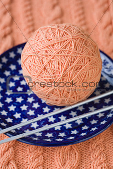 One ball of pink yarn and knitting needles on a blue plate with stars