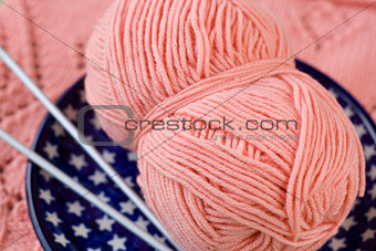 A ball of pink yarn and knitting needles on a blue plate