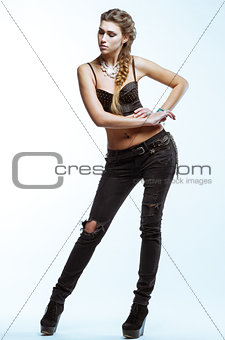 Young blond woman in black top and jeans posing on light backgro
