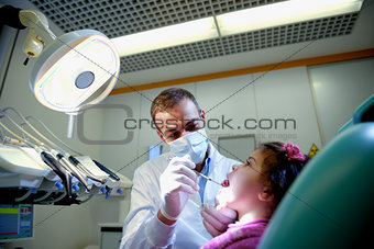 Dentist checking teeth of young girl lying on couch