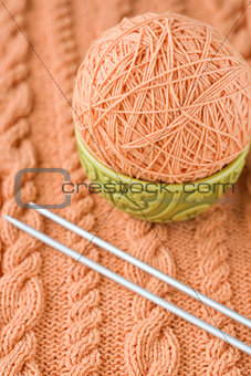 A peach-colored ball of yarn are in the national dish and needles for knitting