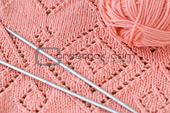 A fragment of a knitted blankets, pink skein of yarn and knitting needles
