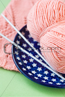 A ball of pink yarn and knitting needles on a blue plate