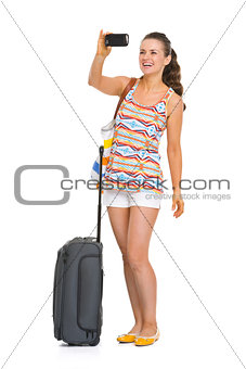 Happy young tourist woman with wheel bag taking photos