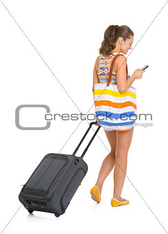 Young tourist woman with wheel bag writing sms . rear view