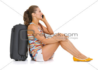 Young tourist woman with wheel bag sitting on floor and talking 