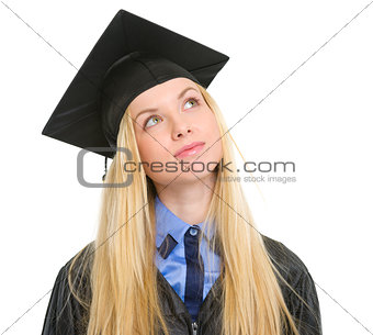 Young woman in graduation gown looking up on copy space
