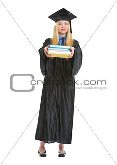 Full length portrait of young woman in graduation gown giving bo
