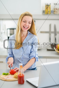Happy teenager girl making sandwich in kitchen and looking in la