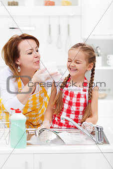 Woman and little girl having fun washing the dishes