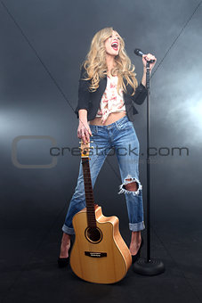 Woman Singing on Stage With Mic and Guitar