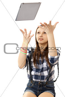 The girl throws in the air tablet PC .  Teenage girl in a plaid shirt and short denim shorts, tosses a PC tablet to the top.