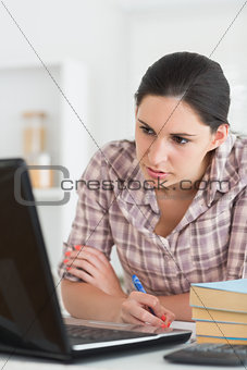Woman writing on a notebook while looking at laptop