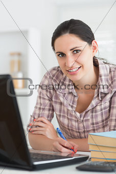 Smiling woman writing on notebook beside laptop