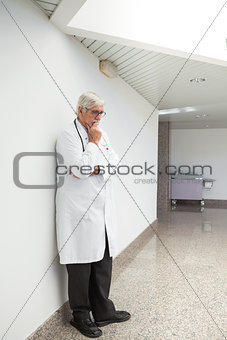 Thinking doctor leaning against wall