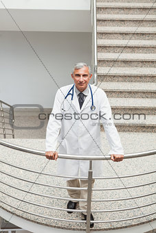 Smiling doctor leaning on the railing of the stairs