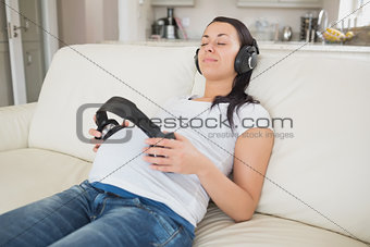 Pregnant woman holding headphones to belly and listening to music