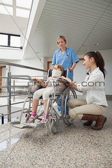 Mother crouching next to her child in wheelchair with nurse pushing it