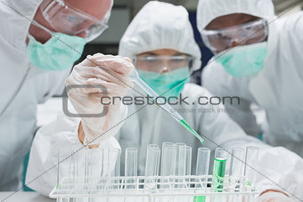 Chemist adding green liquid to test tubes as two others are watching