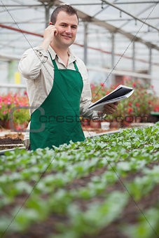 Smiling man on the phone and taking notes in greenhouse