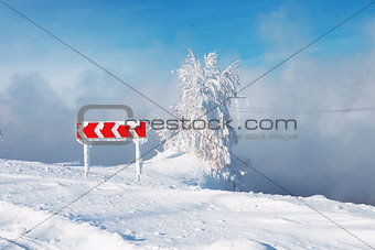 Frozen and snowed guide road sign of turn and tree in a blue foggy background