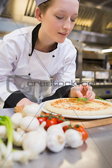 Chef putting basil leaf on pizza