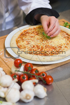 Pizza being garnished with basil leaf