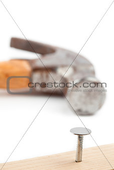 Half nail sticking in a plank and a hammer lying behind