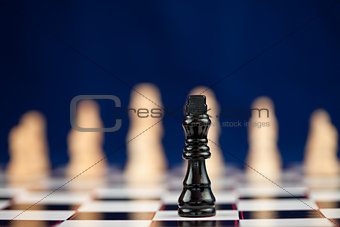 Black chess piece standing at the chessboard white ones behind