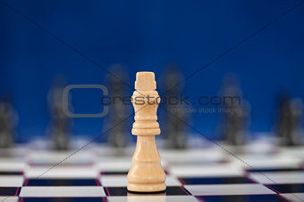 White queen standing at the chessboard while black ones standing behind